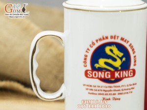 Cốc sứ dáng cao quai nắm men trắng có nắp kẻ chỉ vàng in logo Công ty Song King, 500ml