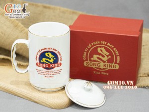 Cốc sứ dáng cao quai nắm men trắng có nắp kẻ chỉ vàng in logo Công ty Song King, 500ml