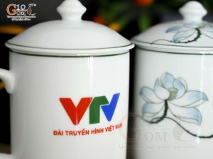 Cốc sứ có nắp men trắng vẽ sen xanh in logo VTV, đường kính 8cm