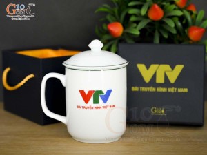 Cốc sứ có nắp men trắng vẽ sen xanh in logo VTV, đường kính 8cm