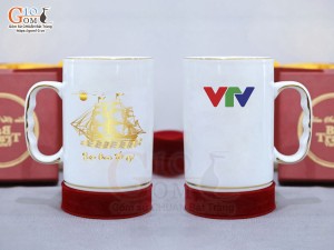 Cốc sứ dáng cao quai nắm men trắng cảnh Thuận Buồm Xuôi Gió vàng kim, in logo VTV, 450ml