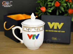 Cốc sứ dáng chóp lửa men trắng họa tiết Trống Đồng vàng kim, in logo VTV 400ml