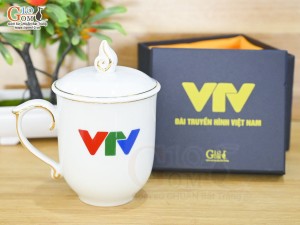 Cốc sứ dáng chóp lửa men trắng kẻ chỉ vàng kim có nắp in logo VTV, 400ml