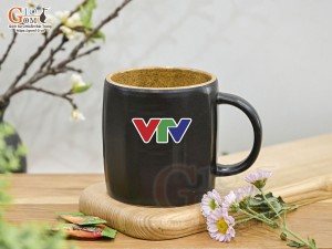 Cốc sứ dáng lục giác quai tròn màu đen cảnh Thuận Buồm Xuôi Gió, in logo VTV