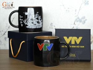 Cốc sứ dáng lục giác quai tròn màu đen cảnh Thuận Buồm Xuôi Gió, in logo VTV