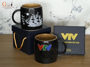 Cốc sứ dáng lục giác quai tròn màu đen cảnh Thuận Buồm Xuôi Gió, in logo VTV
