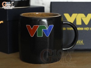 Cốc sứ dáng lục giác quai tròn màu đen cảnh Thuận Buồm Xuôi Gió, in logo VTV
