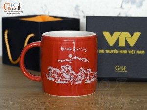 Cốc sứ dáng lục giác quai tròn màu đỏ cảnh Mã Đáo Thành Công, in logo VTV