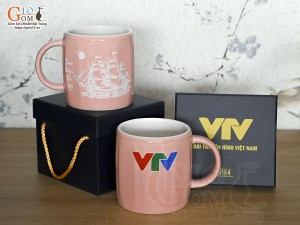 Cốc sứ dáng lục giác quai tròn màu hồng cảnh Thuận Buồm Xuôi Gió, in logo VTV