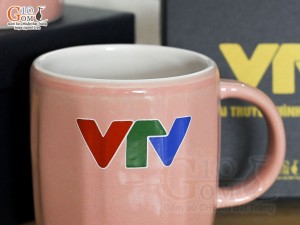 Cốc sứ dáng lục giác quai tròn màu hồng cảnh Thuận Buồm Xuôi Gió, in logo VTV