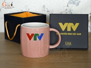 Cốc sứ dáng lục giác quai tròn màu hồng cảnh Thuận Buồm Xuôi Gió, in logo VTV