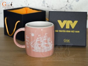 Cốc sứ dáng lục giác quai tròn màu hồng cảnh Thuận Buồm Xuôi Gió, in logo VTV