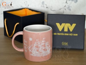 Cốc sứ dáng lục giác quai tròn màu hồng cảnh Thuận Buồm Xuôi Gió, in logo VTV